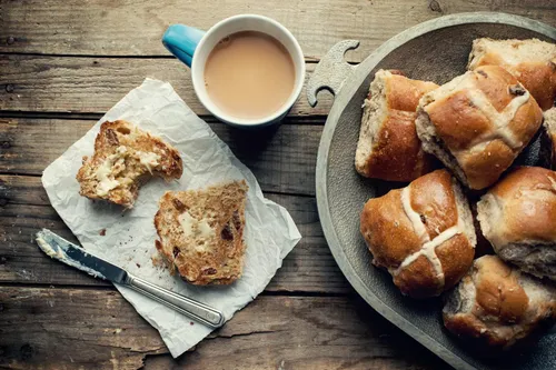 A plate of hot cross buns with a cup of tea